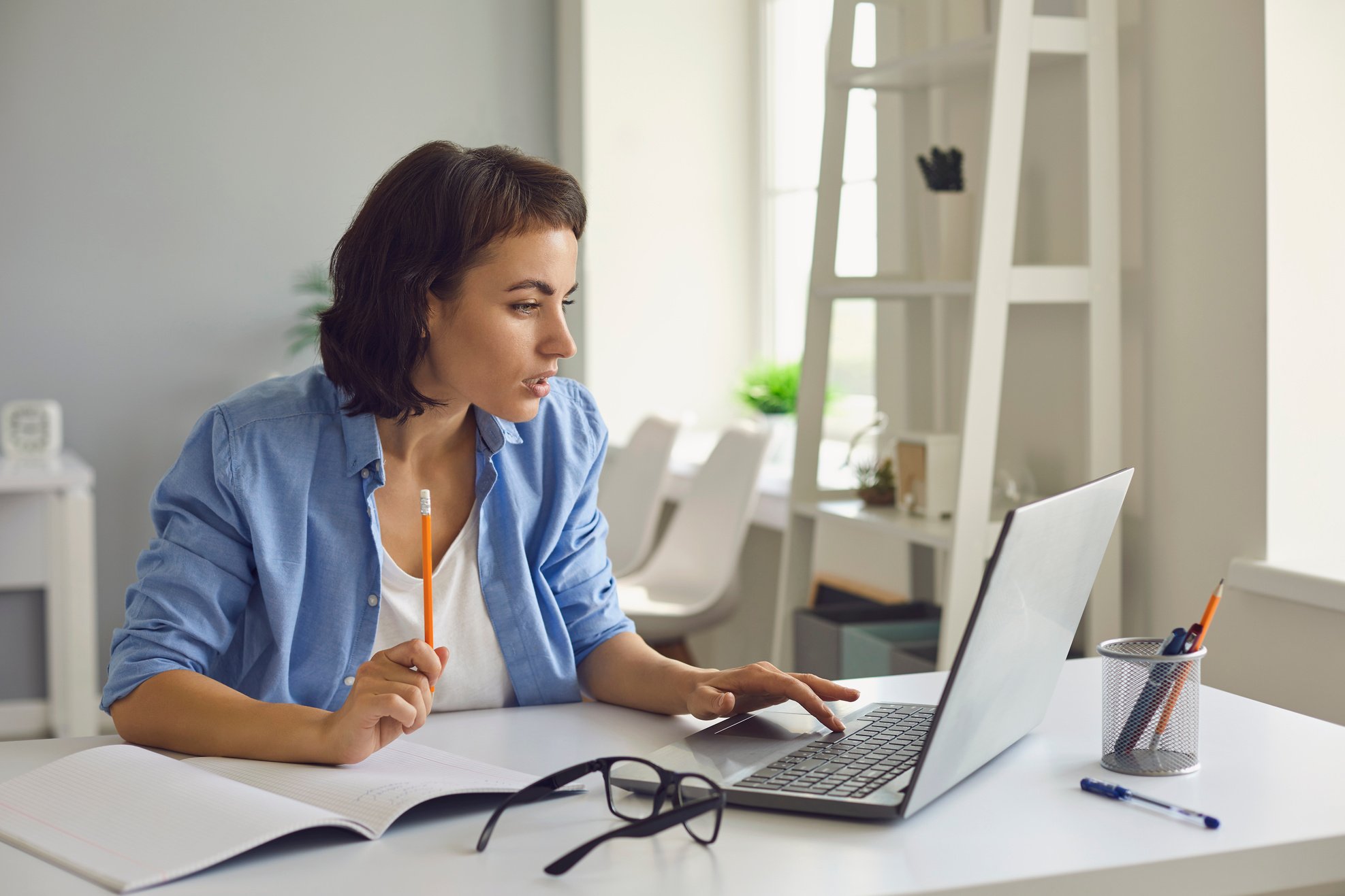 Woman Talking to Somebody and Making Notes during Online Conversation on Laptop at Home